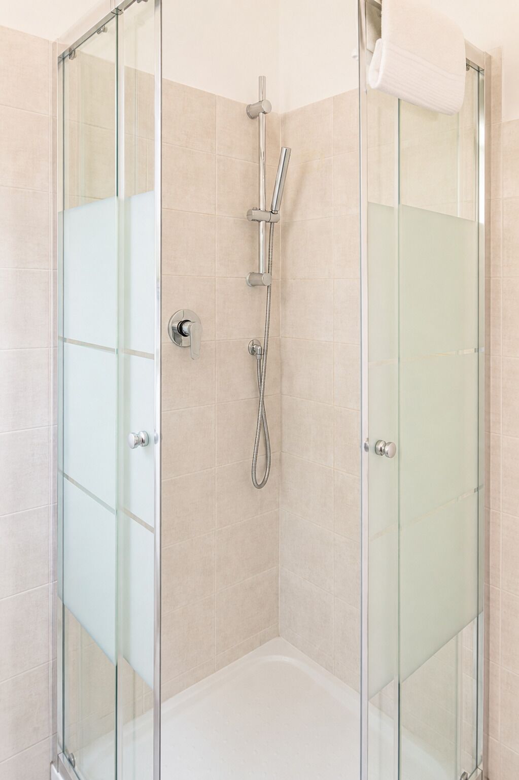 A glass-enclosed shower stall with a handheld showerhead and a wall-mounted faucet.
