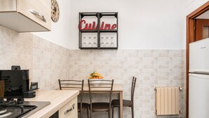 A kitchen with a dining table, chairs, a clock, a wine rack, and a refrigerator.
