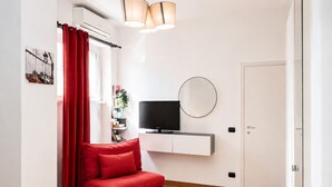 A modern living room with a red sofa, a flat-screen TV, a round mirror, and a bookshelf.