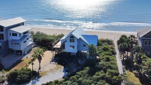 A coastal property with multiple buildings, including a prominent house with a blue roof and a smaller structure with a white roof. The property is adjacent to a beach with visible waves and a clear sky. - Beachfront - Community Pool/Pickleball Access! (St. George Island)