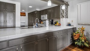 Una cocina moderna con armarios grises, una encimera blanca, microondas integrado e iluminación colgante.