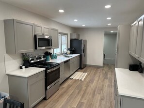 A modern kitchen with grey cabinets, stainless steel appliances, and a white countertop.