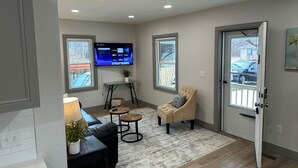 Ein Wohnzimmer mit Fernseher, Sofa, Sessel und einem kleinen Tisch.