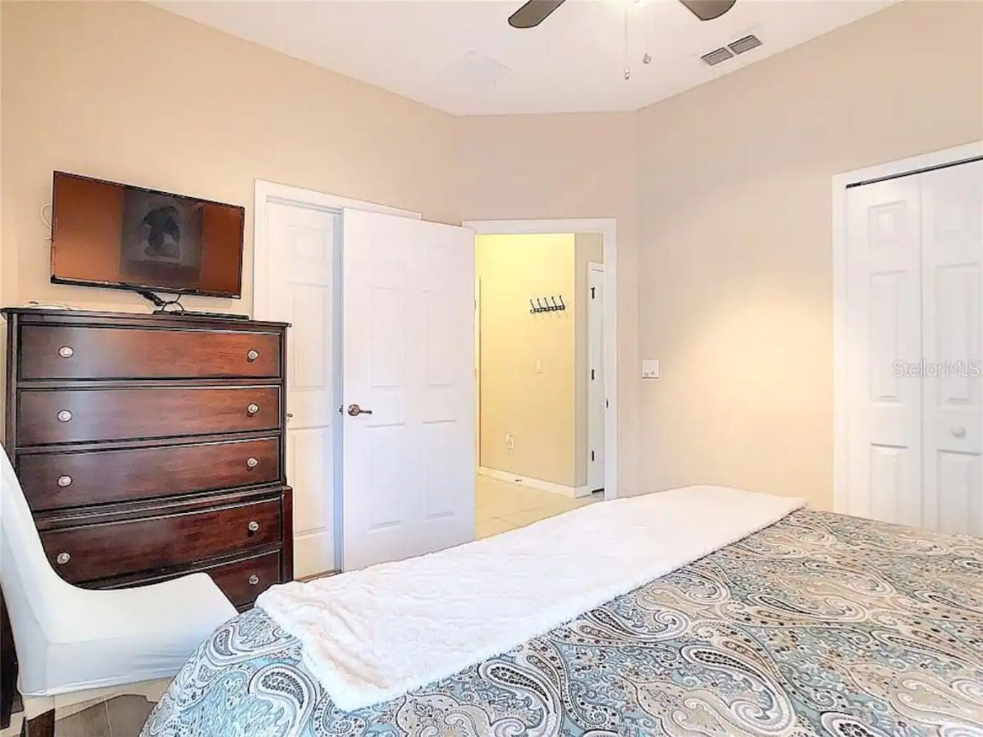 Ein Schlafzimmer mit Bett, Kommode und Fernseher an der Wand.