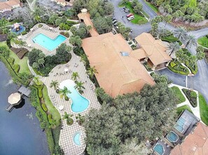 An aerial view of a residential area with multiple swimming pools, a large house, and surrounding greenery.