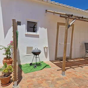A patio with a barbecue grill, potted plants, and a window.