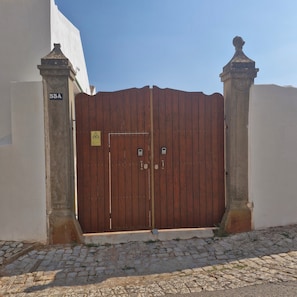 A closed wooden gate with a warning sign, flanked by two columns, leading to a cobblestone path.