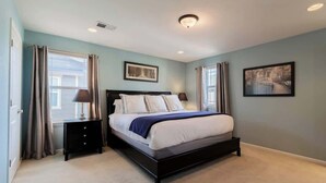 Une chambre à coucher avec un lit, deux tables de chevet, un luminaire au plafond et deux tableaux encadrés accrochés au mur.