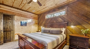 A bedroom with a wooden ceiling, a bed with striped bedding, a nightstand, a dresser, and a window with a view of trees.