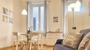Un saló acollidor amb un sofà gris, una taula de menjador amb caires i una finestra amb cortines.