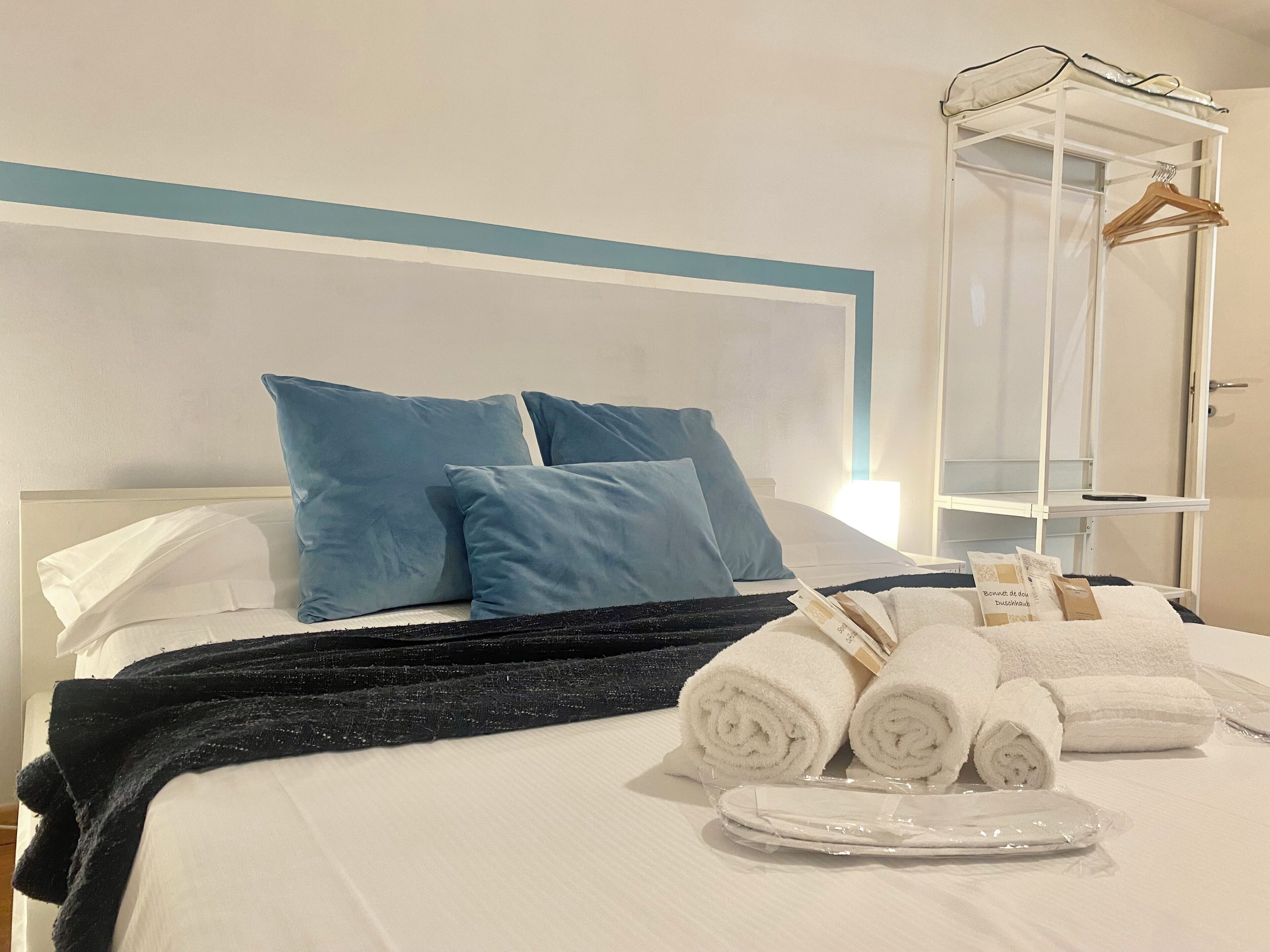 A neatly made bed with blue pillows, a black throw blanket, and rolled white towels.