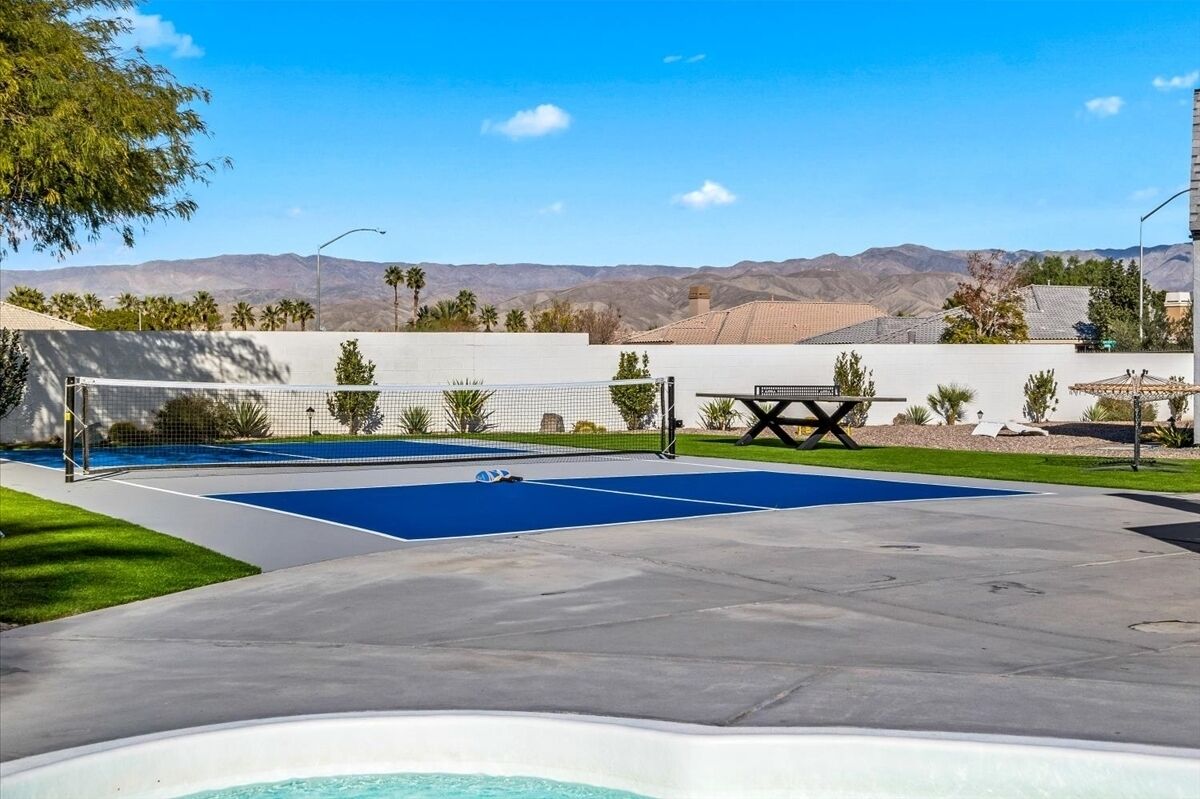 Un espace piscine doté d’un court de tennis protégé par un filet, d’un jacuzzi et offrant une vue sur les montagnes.