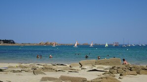 A beach with rocks in the foreground and sailboats on the water. - Holiday Home in Paimpol near Beaches (Paimpol)
