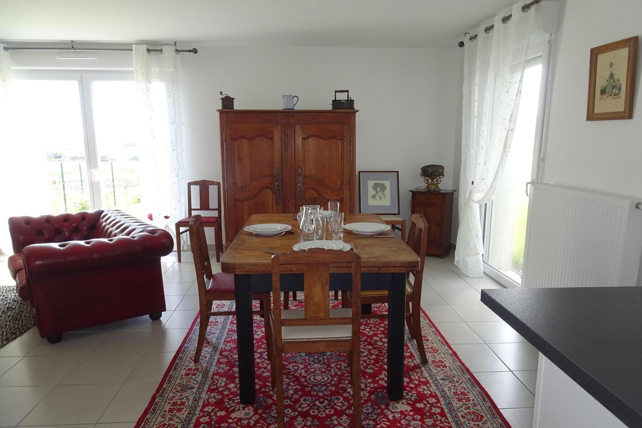A dining area with a wooden table set for four, a red sofa, and a cabinet with a picture frame.