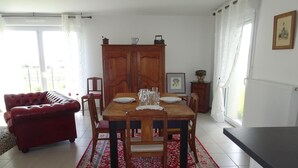 A dining area with a wooden table set for four, a red sofa, and a cabinet with a picture frame. - Holiday Home in Paimpol near Beaches (Paimpol)