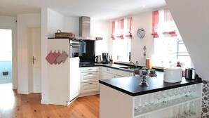 A modern kitchen with white cabinets, a black countertop, and a built-in wine rack. - Ferienwohnung in Wyk auf Foehr (Wyk auf Föhr)