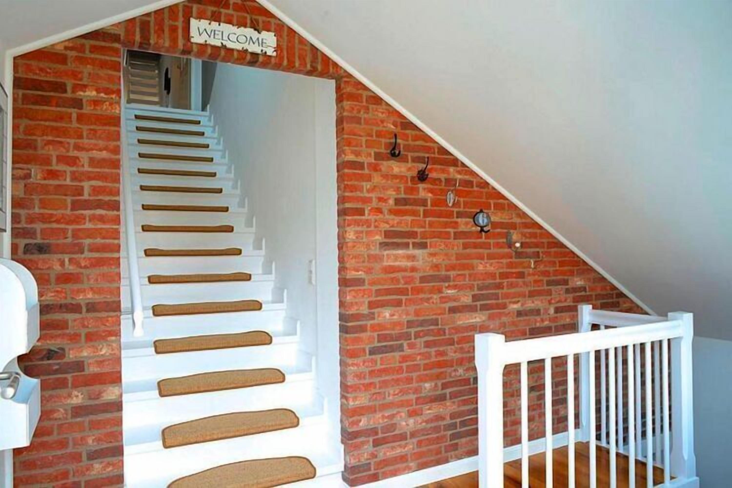 Eine Treppe mit weißen Stufen führt zu einer Zwischenebene, an der eine Ziegelwand und ein weißes Geländer zu sehen sind.