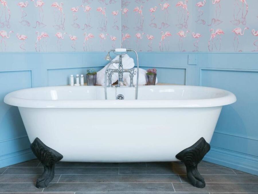 A clawfoot bathtub in a bathroom with blue walls and a floral wallpaper pattern.
