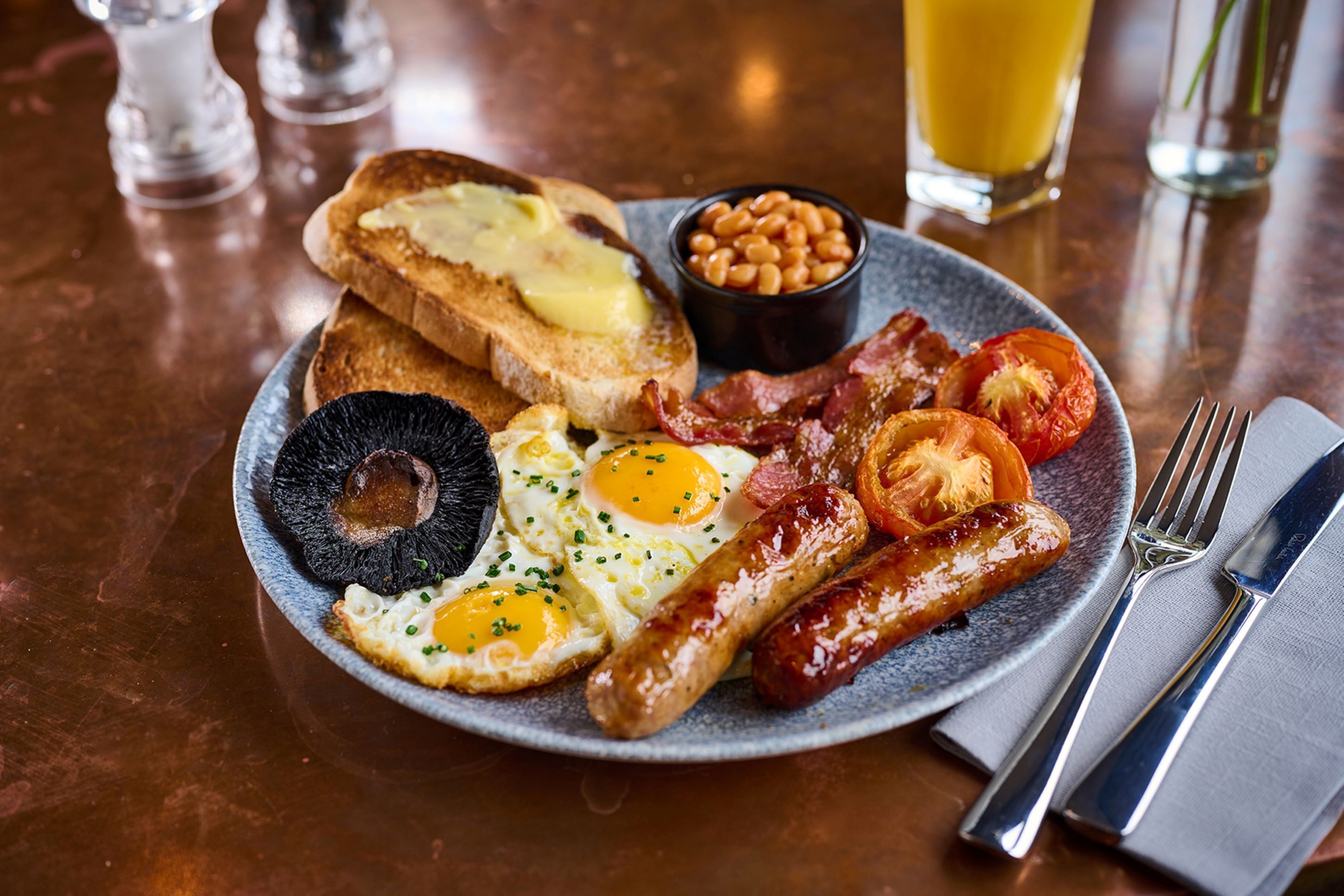 En tallerken med morgenmad bestående af æg, bacon, pølser, ristet brød, bønner og tomater.