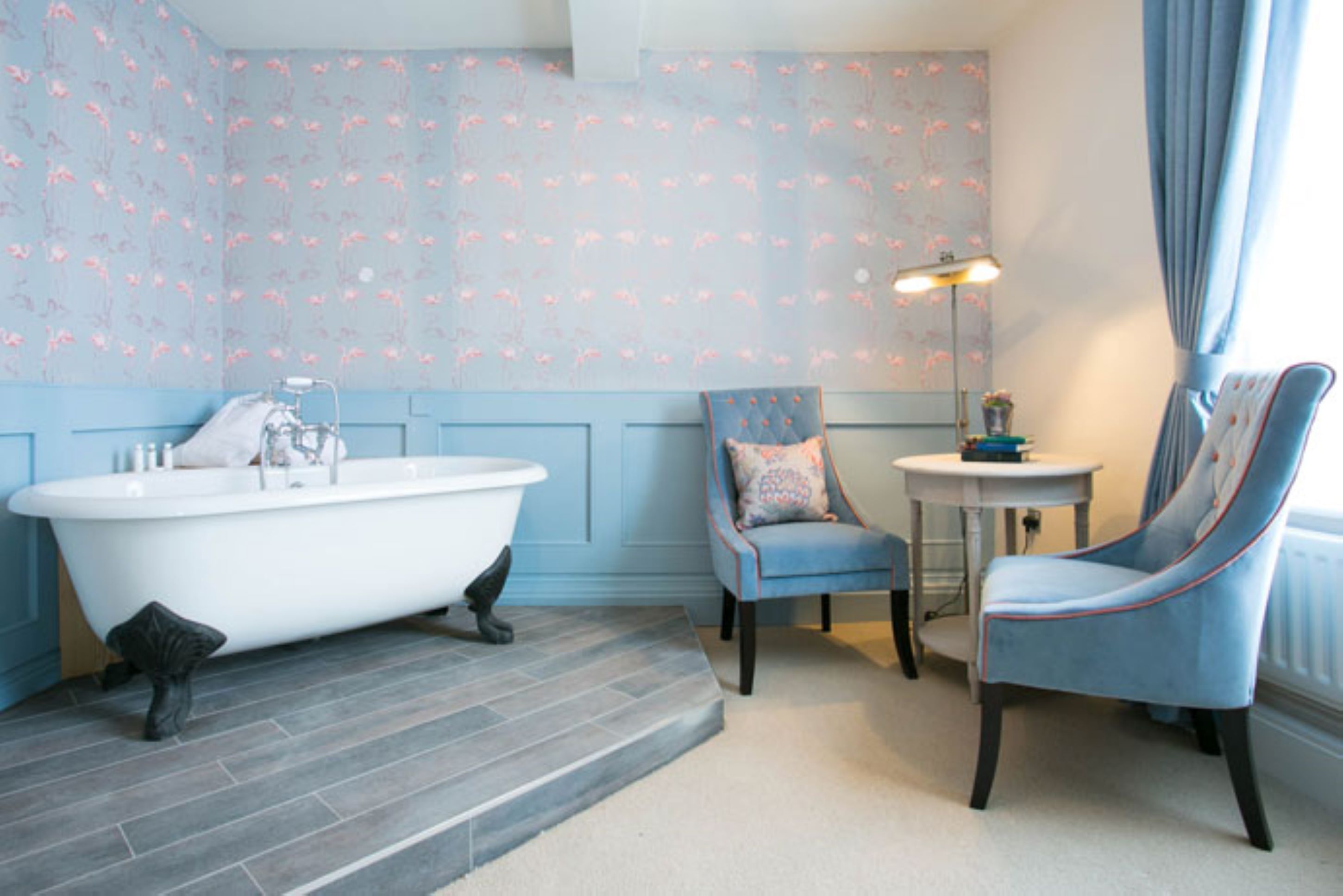 A bathroom with a clawfoot bathtub, a chair, a small table, and a lamp.