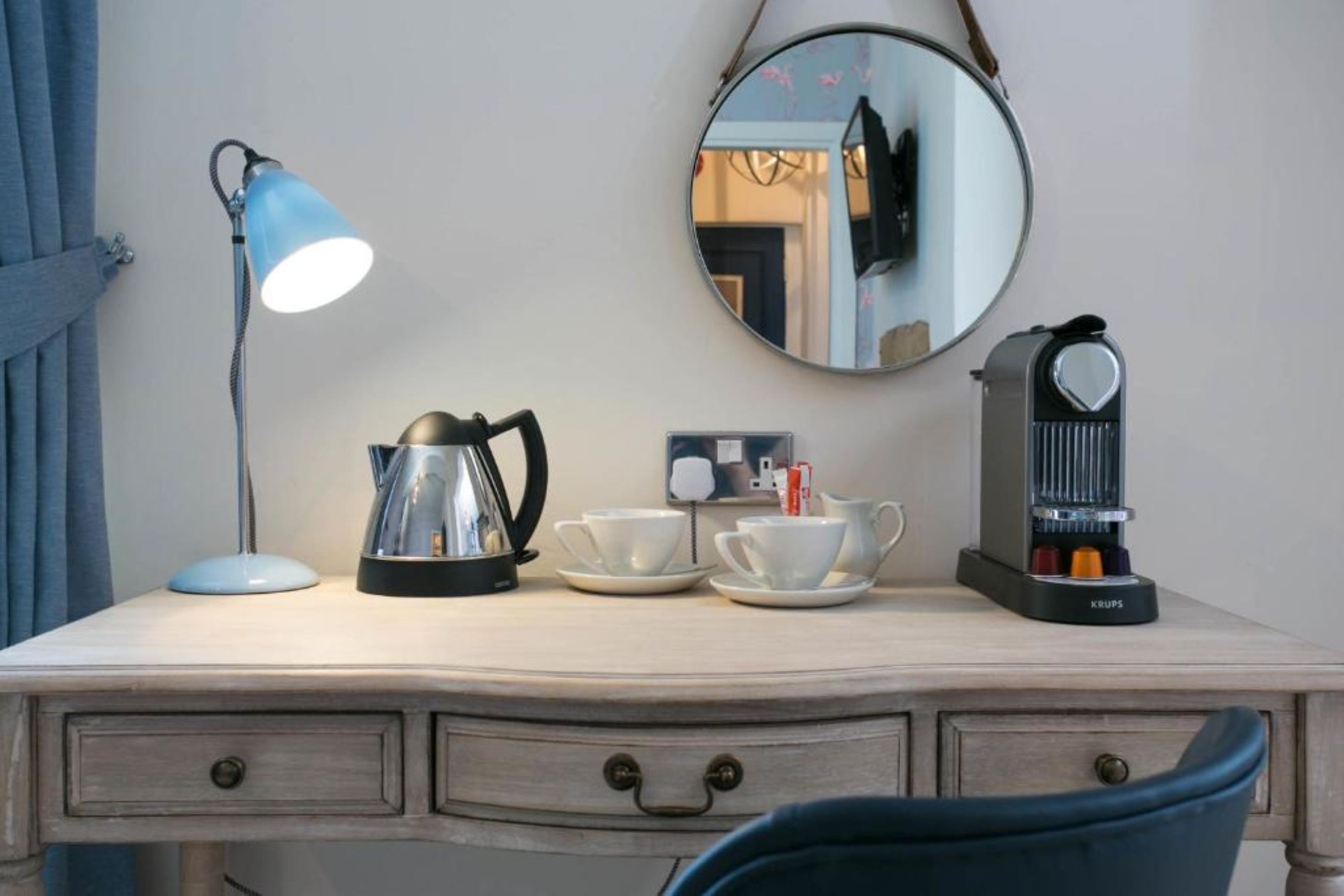 Een houten bureau met een lamp, een koffiezetapparaat en kopjes.