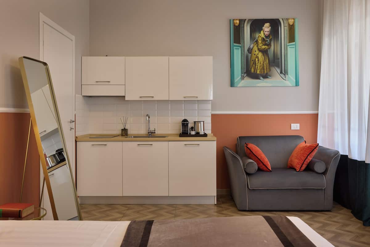 A compact room with a kitchenette, a sofa, and a painting on the wall.