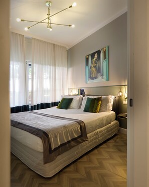A spacious bedroom with a large bed, a modern chandelier, and a painting on the wall.
