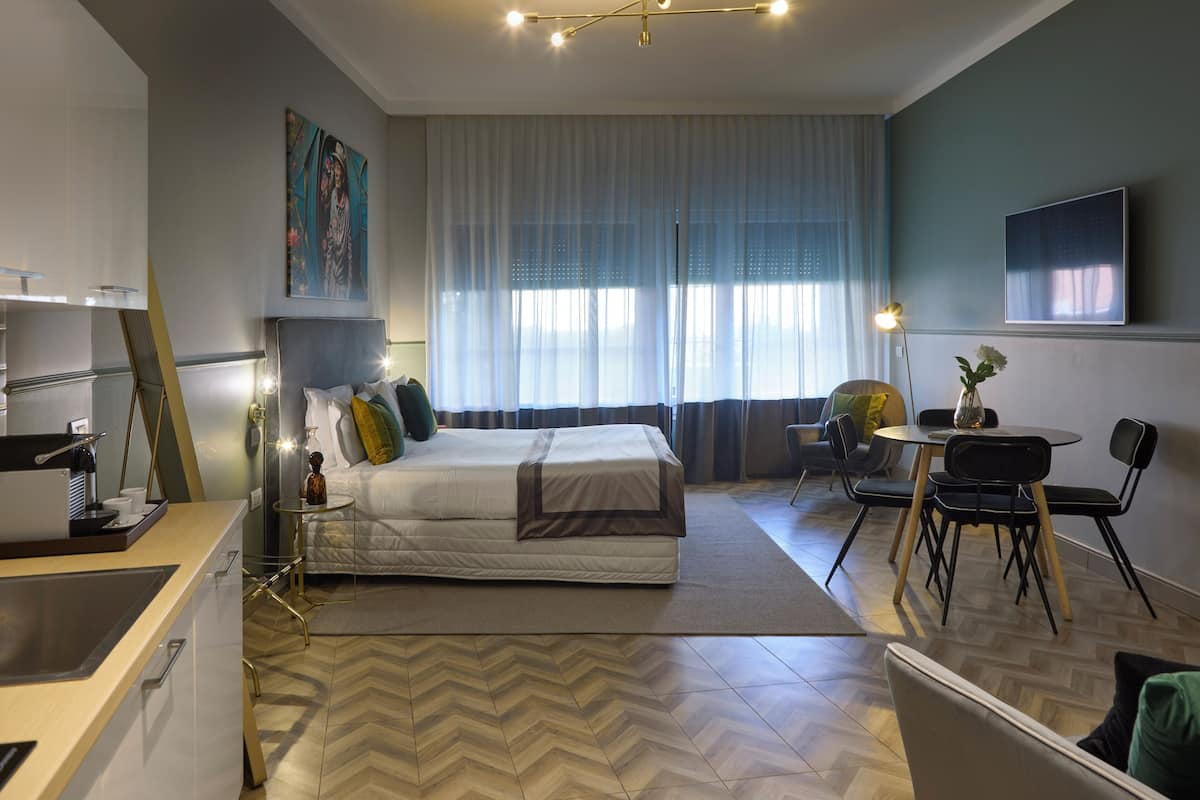 A modern hotel room with a bed, a desk, a chair, a small table, and a TV on the wall.