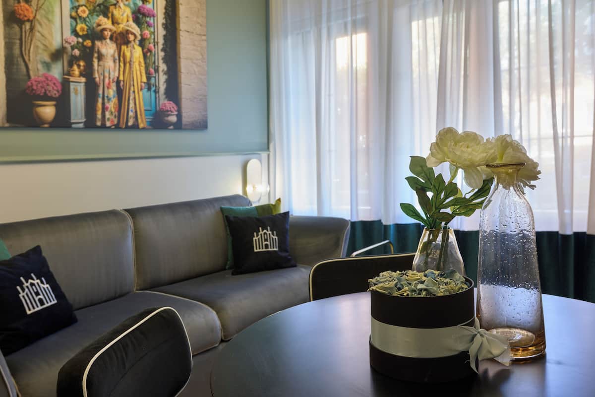 A modern living room with a leather sofa, a round table with a vase of flowers, and a painting on the wall.
