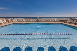 En pool med utsikt över havet, omgiven av solstolar och ett livräddartorn.