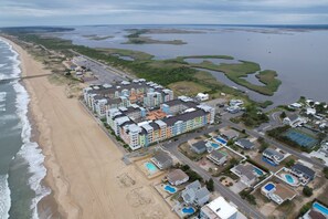 An aerial view of a coastal residential area with multi-story buildings, a beach, and a marina. - Book A Sandbridge Retreat 222 A | 3-Bedroom Sandbridge Condo (Virginia Beach)