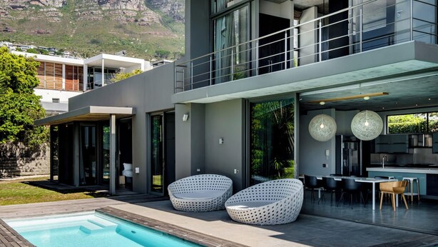A modern two-story house with a swimming pool, outdoor seating, and a view of mountains.