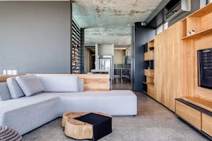 A modern living room with a grey sectional sofa, a wooden coffee table, and built-in wooden shelving with a flat-screen TV.