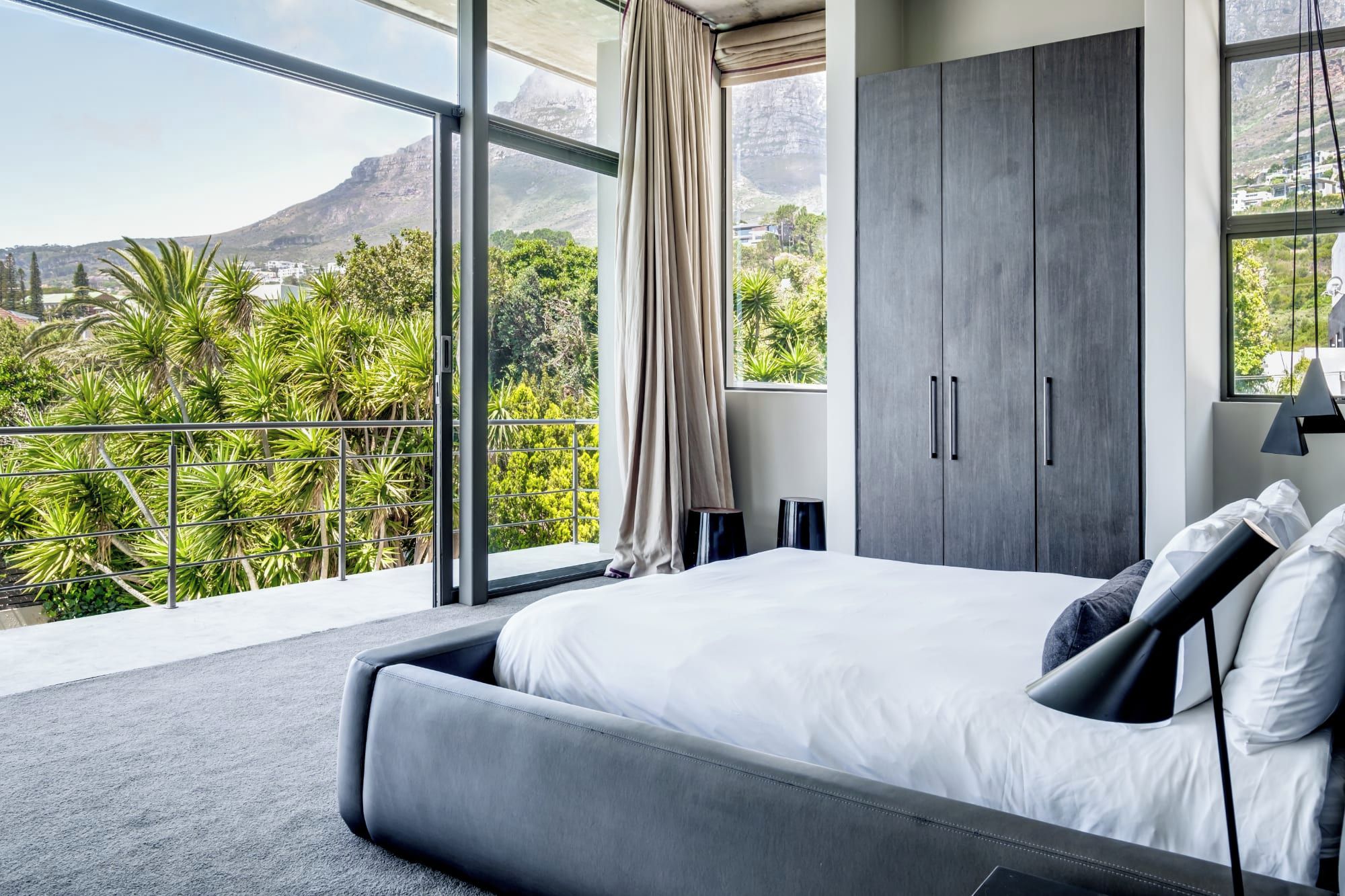 A modern bedroom with a large bed, a wardrobe, and a balcony with a mountain view.