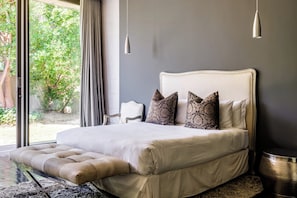 A bedroom with a large bed, a view of greenery outside, and a modern pendant light.