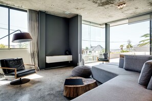 A modern living room with a large window, a sofa, a chair, a lamp, and a small wooden table.