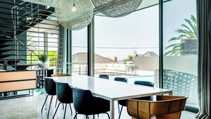 A modern dining area with a long table, chairs, and a view of the outside.
