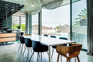 A modern dining area with a long table, chairs, and a view of the outside.