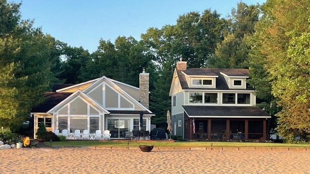 Une propriété au bord du lac, dotée d’un quai s’avançant dans l’eau, d’un patio couvert et d’une grande maison avec une cheminée en pierre.