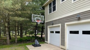 Un garage attenant à une maison, avec deux portes de garage blanches, un panier de basketball et une allée en béton.