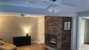 Une chambre avec une cheminée en briques, un ventilateur de plafond, un lit, une table de chevet et une commode.