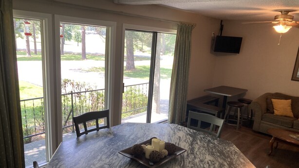 Un espace repas avec une table en marbre, des chaises et une vue sur un espace extérieur verdoyant, grâce à de grandes fenêtres.
