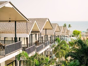 Fila de habitaciones de hotel frente a la playa, con balcones, palmeras y vista al océano.