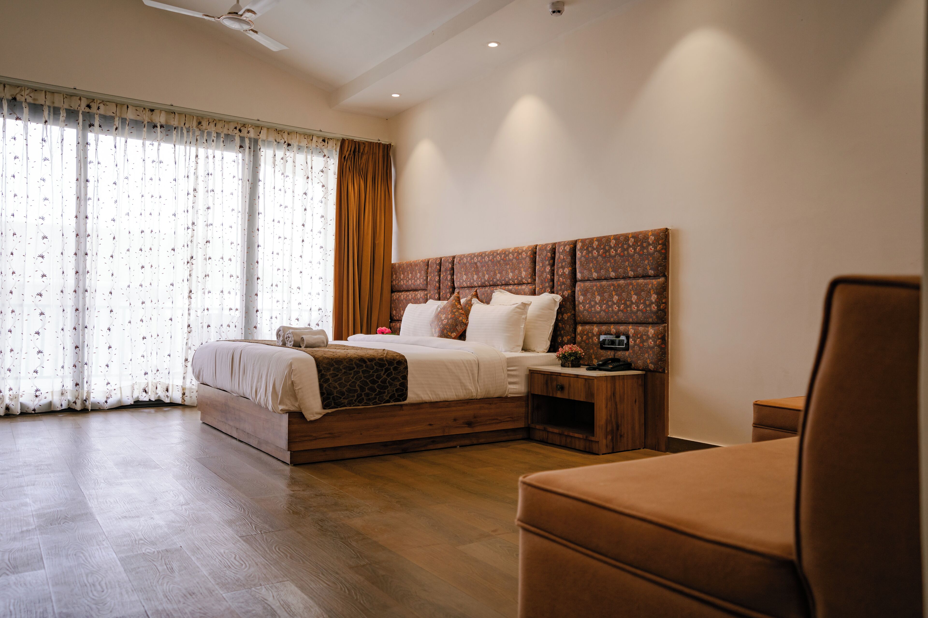 Un dormitorio con cama de madera, mesita de noche, silla y ventana con cortinas.