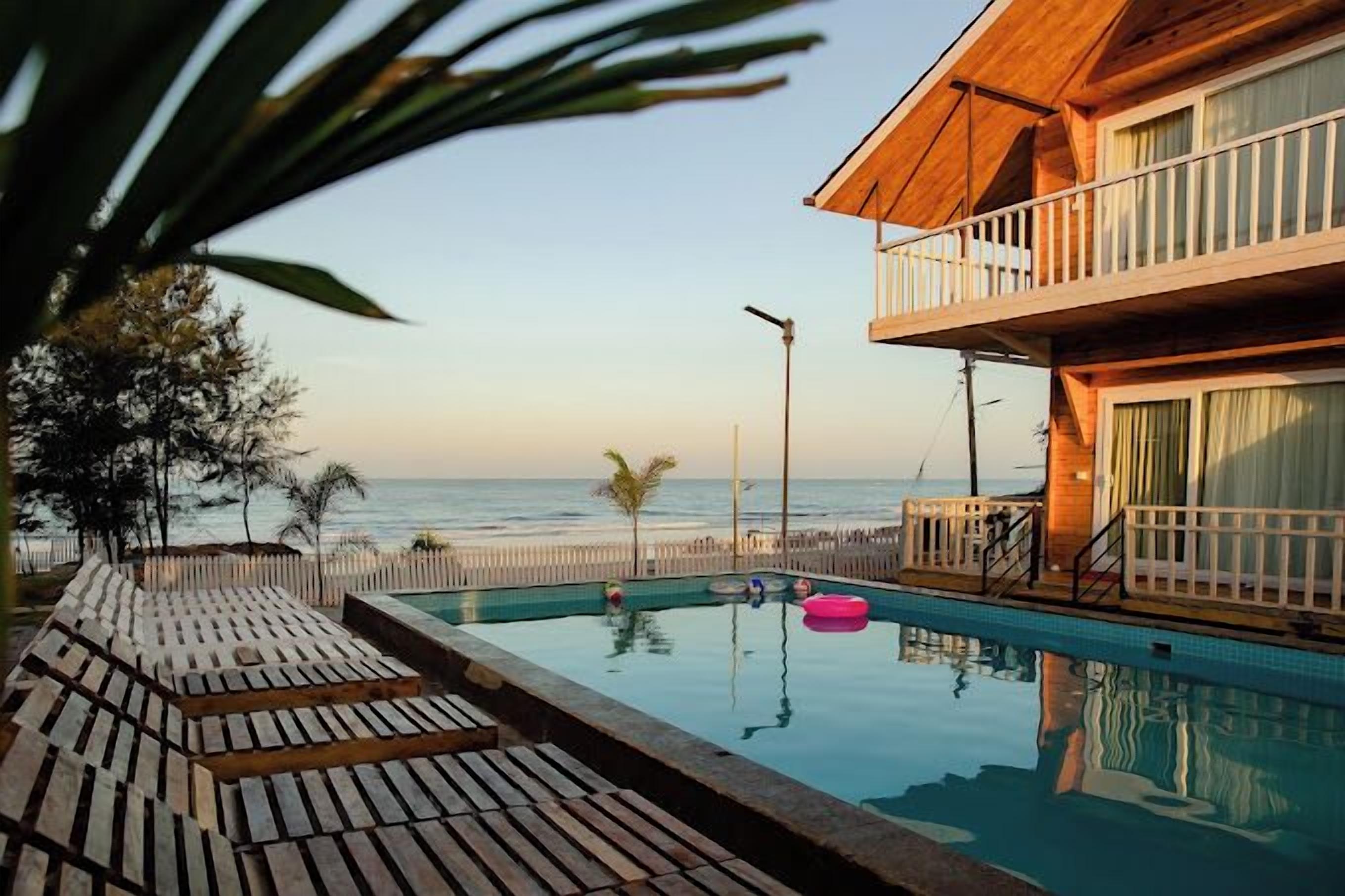 A wooden deck with a pool, a balcony, and a view of the ocean.