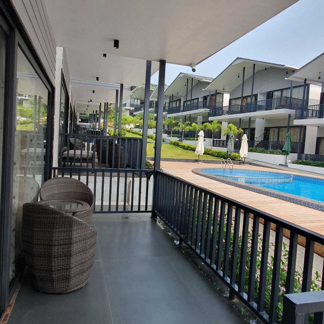 A hotel balcony with a pool, wicker chairs, and a view of other hotel buildings.