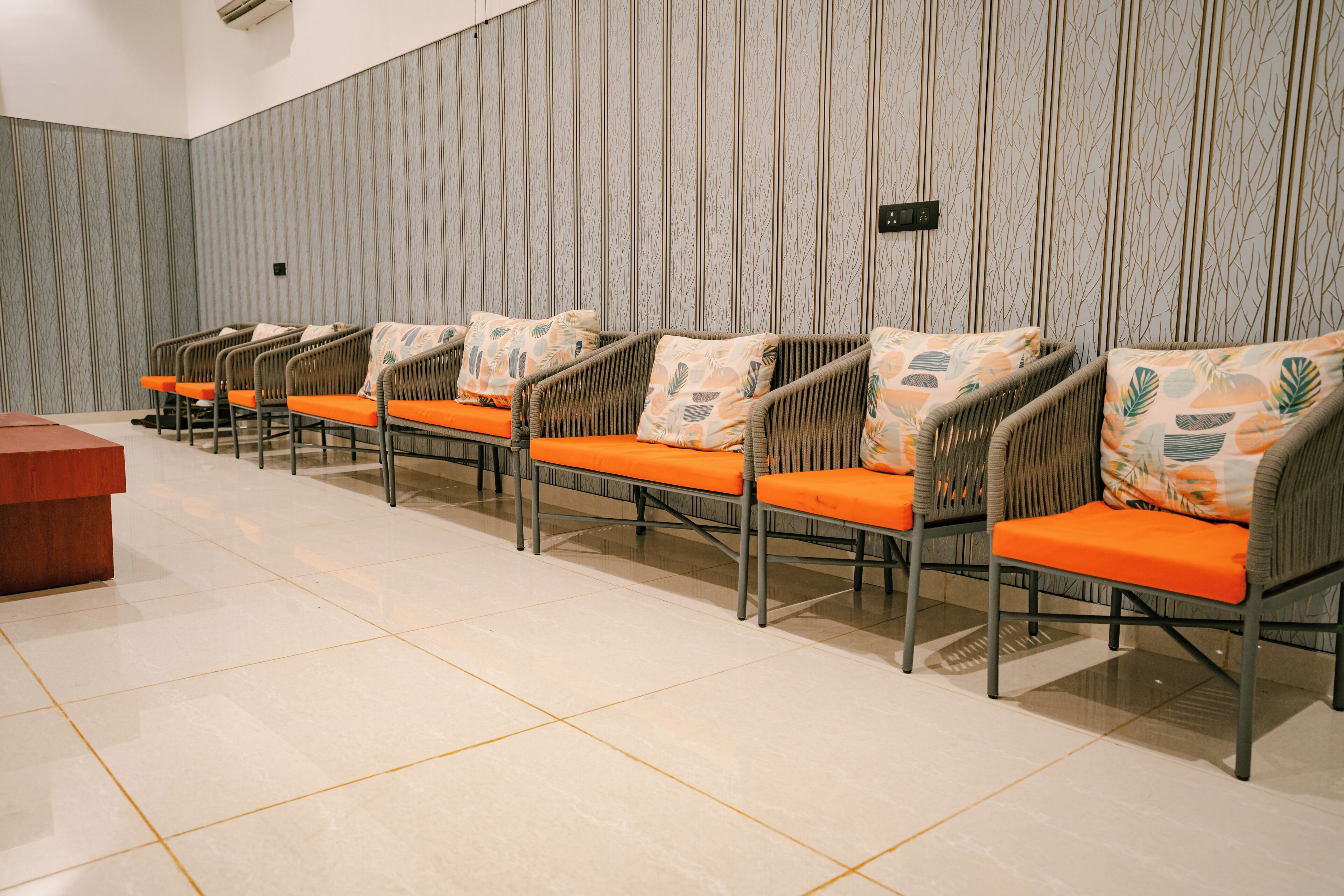 A row of wicker chairs with orange cushions and a wooden desk in a room with striped wallpaper.