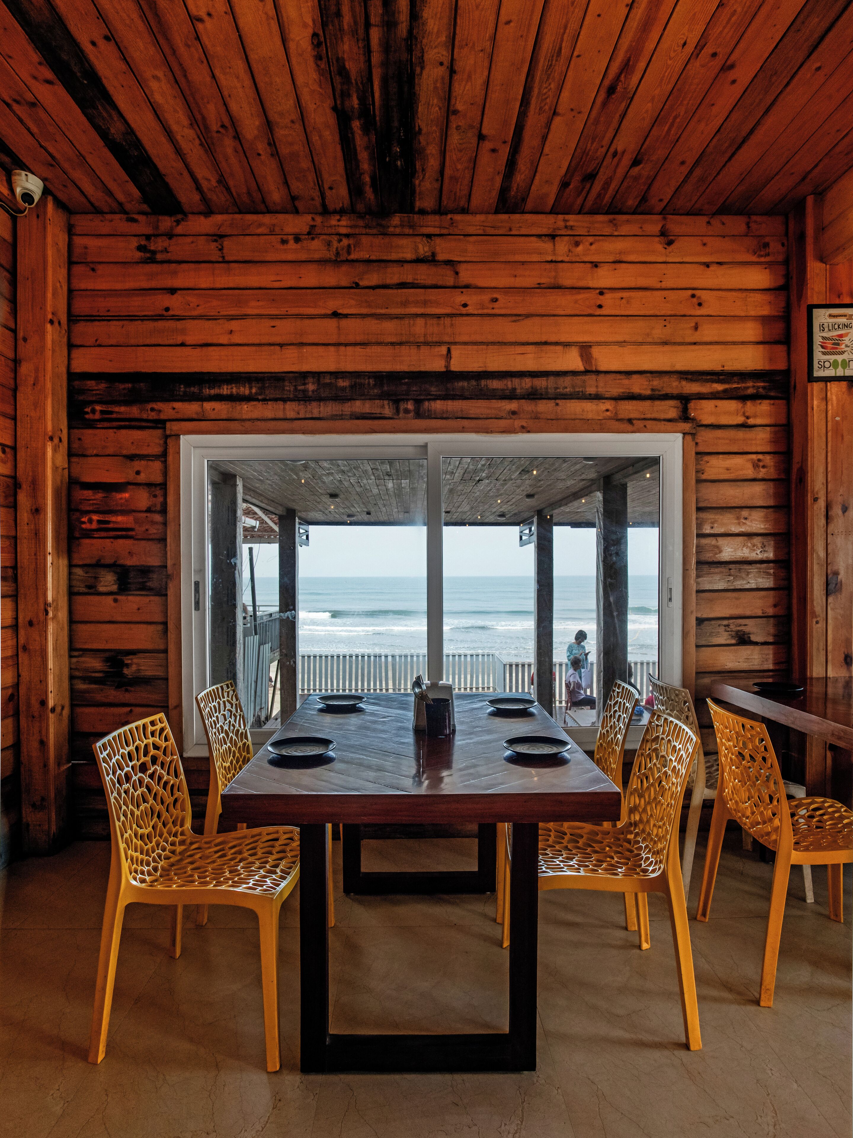 Un interior de madera con una mesa y sillas, vista al océano y un cartel en la pared.