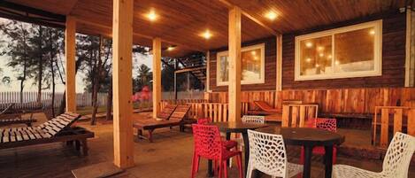 Une terrasse extérieure couverte, dotée d’un plancher en bois, d’une table avec des chaises et d’une clôture en bois en arrière-plan.