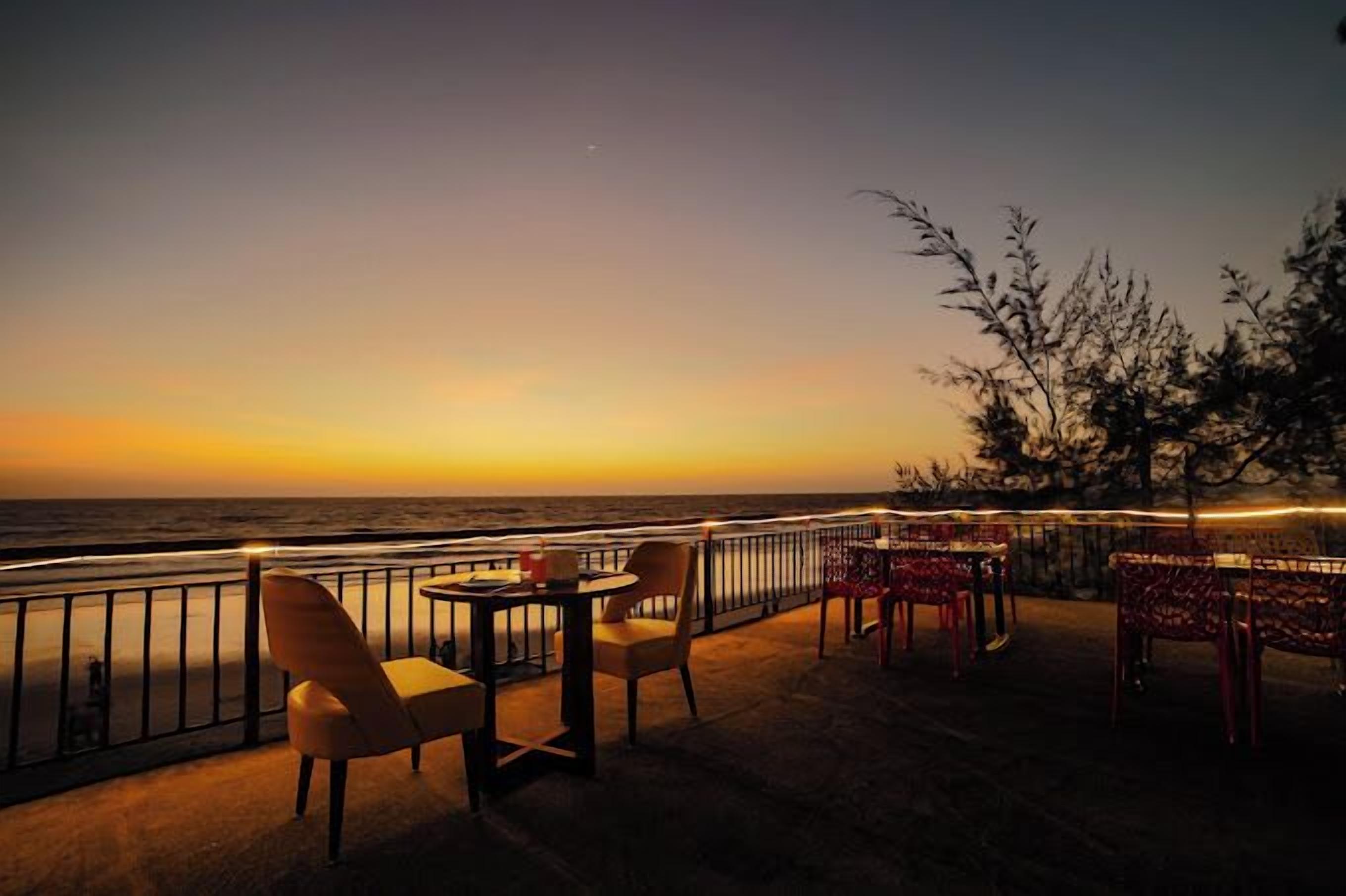 Un restaurant en bord de mer avec une terrasse, une vue sur l’océan et une rambarde.